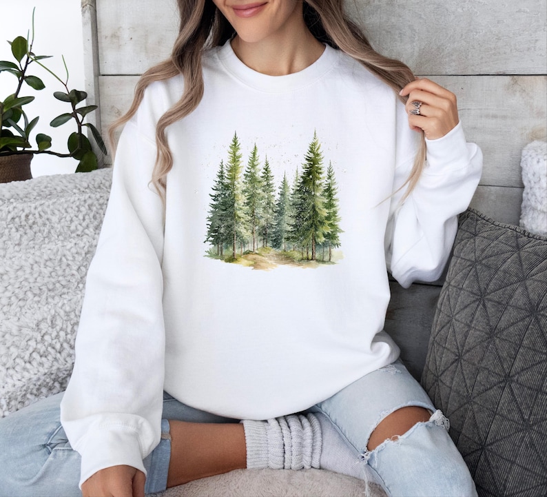 May include: White sweatshirt with a watercolor design of a forest with green trees.