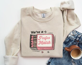 May include: A beige sweatshirt with a graphic of a matchbox that says "We're a Perfect Match".