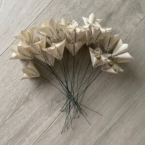 May include: A bouquet of paper flowers made from book pages, with black wire stems. The flowers are arranged in a fan shape, with the stems gathered together at the bottom.