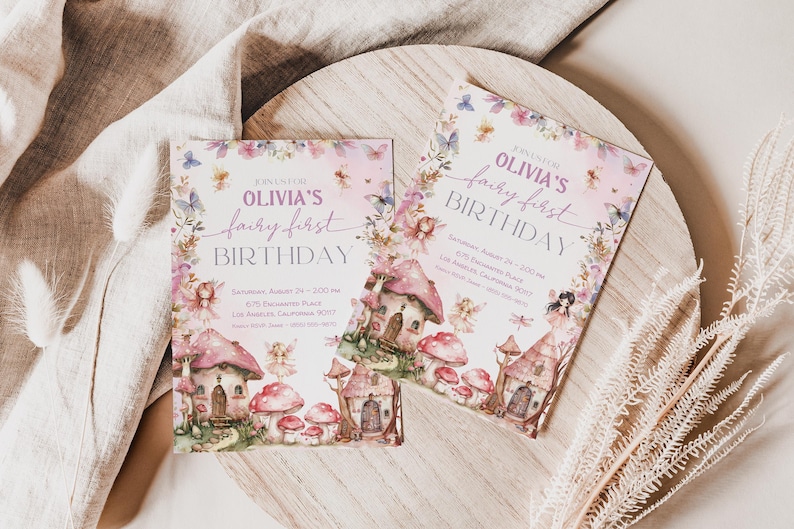 May include: Two pink and purple fairy-themed first birthday party invitations with a watercolor design featuring a fairy house, mushrooms, and flowers. The text on the invitations reads "Olivia's fairy first birthday".