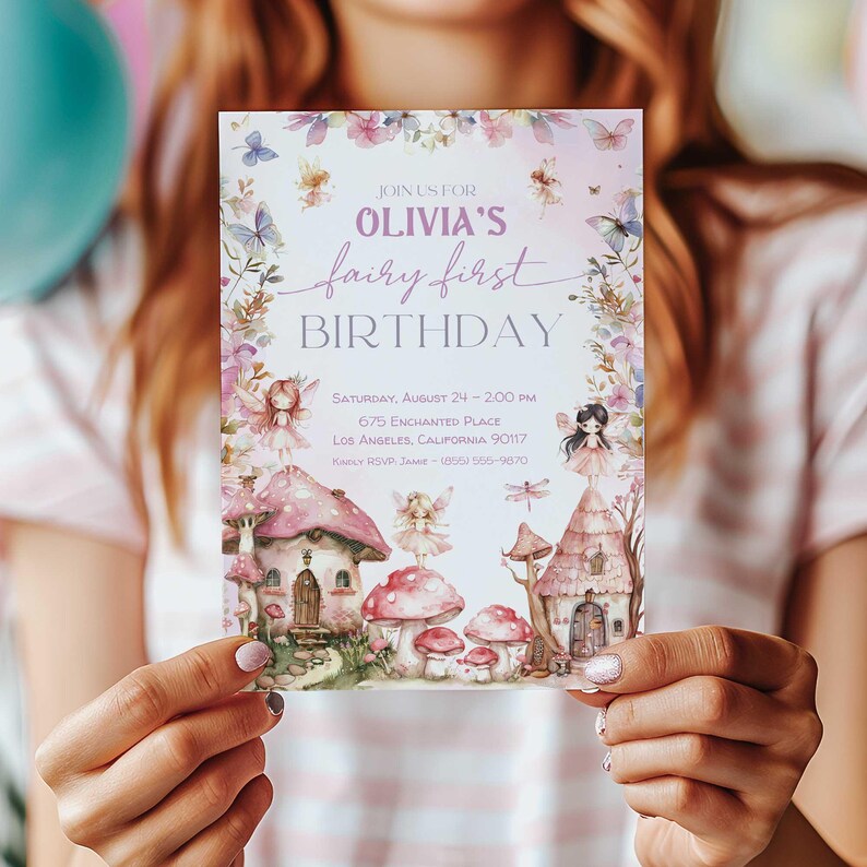 May include: A pink and purple fairy-themed birthday invitation with a watercolor illustration of a fairy village, mushrooms, and butterflies. The text reads "Join us for Olivia's fairy first birthday. Saturday, August 24 - 2:00 PM, 675 Enchanted Place, Los Angeles, California 90117. Kindly RSVP Jaime (800) 555-9870."