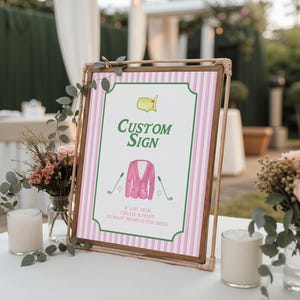 Puede incluir: Un letrero personalizado con un fondo a rayas rosas y blancas y un marco de madera marr&oacute;n. El letrero presenta un dise&ntilde;o tem&aacute;tico de golf con una chaqueta rosa, palos de golf y el texto "Custom Sign". El letrero se muestra sobre una mesa blanca con arreglos florales.