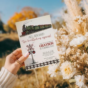 May include: A birthday party invitation featuring a vintage train illustration. The invitation reads "All Aboard the birthday express!" and includes details for a party celebrating Grayson's fifth birthday. The design incorporates a railroad crossing sign.