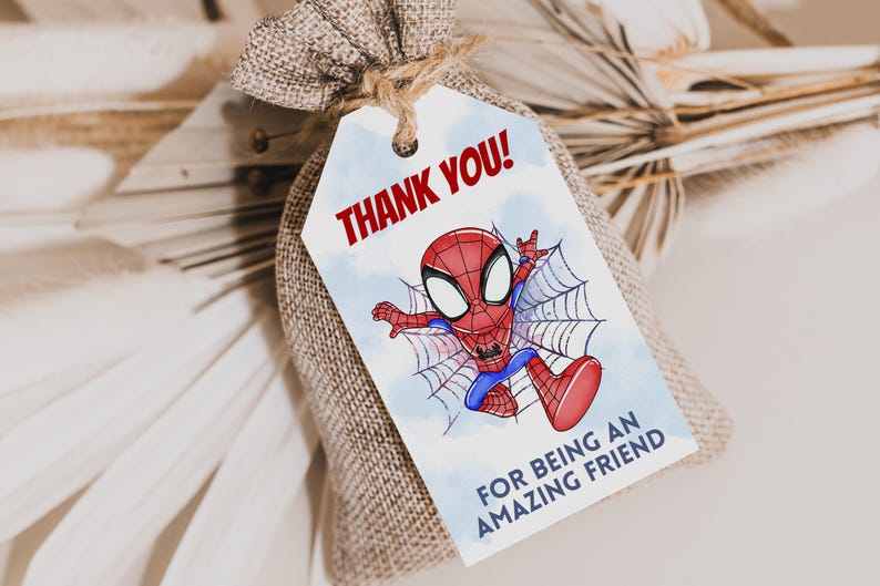May include: A white thank you tag with a cartoon illustration of Spiderman in a red and blue suit swinging on a web. The tag says "Thank You!" in red letters and "For being an amazing friend" in blue letters.