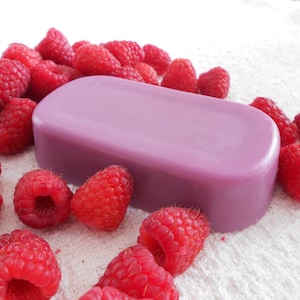 May include: A purple bar of soap surrounded by red raspberries on a white surface.
