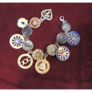May include: A charm bracelet with a variety of buttons and charms, including a heart, a flower, a crown, and a star. The bracelet is made of silver and gold metal and has a blue and white color scheme.