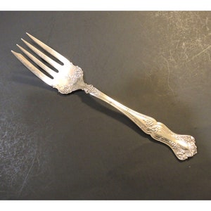 May include: A silver fork with an ornate handle featuring a floral design. The fork has four tines and a polished finish.