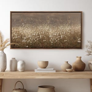 May include: A framed canvas art print depicts a field of white wildflowers in a sepia tone. The artwork is in a dark brown wooden frame. The image is displayed above a wooden table with decorative vases and bowls.