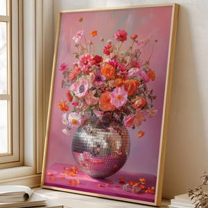 Op de afbeelding: Een boeket met roze, rode en oranje bloemen in een zilveren discobalvaas tegen een roze achtergrond.