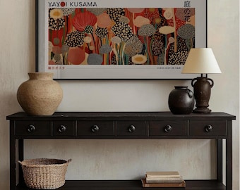 May include: A black console table with four drawers and a lower shelf. The table is decorated with a framed print of a colorful abstract painting by Yayoi Kusama, two ceramic vases, a lamp with a cream-colored shade, and a woven basket.