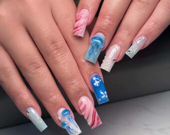 May include: A set of long, square acrylic nails. Designs include blue jellyfish, white flowers, and pink and red swirls. Some nails have small silver embellishments. The nails are a vibrant display of nail art.