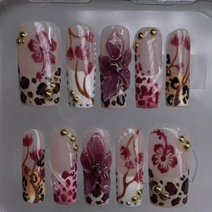 May include: Ten fake fingernails with a variety of designs. The designs include pink and white flowers, leopard print, and gold accents.
