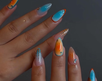 May include: A set of long, almond-shaped acrylic nails. The nails feature a gradient design with orange and blue hues, accented with small rhinestones and orange outlines. Some nails have a dotted pattern.
