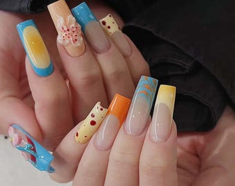 May include: Long, square-shaped nails with a variety of colourful designs. Some nails have a blue base with a yellow sun design, others have a yellow base with red polka dots, and others have a light orange base with a blue and white swirl design.