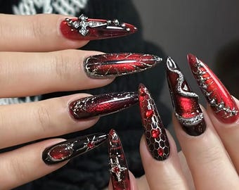 May include: Red and black stiletto nails with intricate silver designs, including a snake, cross, and geometric patterns.