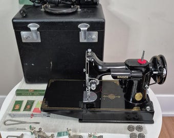 May include: A black Singer sewing machine with gold detailing, accompanied by a black carrying case, a foot pedal, and various metal sewing attachments, bobbins, and small green boxes labeled Singer, all arranged on a white surface.