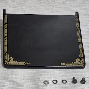 May include: Black rectangular sewing machine base with gold decorative trim and corner designs. Includes several small washers and screws. The base has a smooth, glossy finish.
