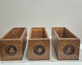 May include: Three rectangular wooden boxes with a natural wood finish. Each box has a carved circular design on the front. The boxes are open at the top and appear to be empty.