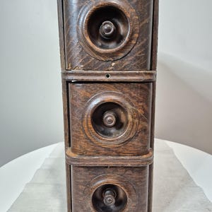 May include: A vintage wooden cabinet with three drawers. Each drawer has a circular, carved design around the knob. The cabinet is made of dark-stained wood, showing the natural grain. The piece has a classic, antique aesthetic.