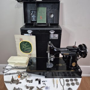 May include: A black Singer sewing machine with a matching black carrying case, a power cord, a foot pedal, a manual titled Smart Fashion Stitches, a white plastic accessory box, metal scissors, and an assortment of various metal sewing machine feet, bobbins, and small tools arranged on a white surface.