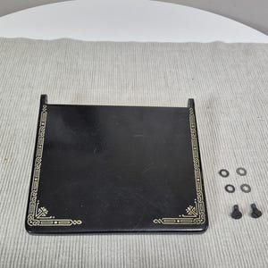 May include: A black rectangular sewing machine base with decorative gold trim. The base has two vertical supports and is accompanied by several small washers and screws.
