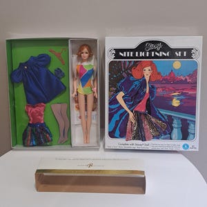 May include: Vintage Barbie doll and fashion set. The set includes a doll in a colorful swimsuit, a blue dress, a pink top with a sequined skirt, and a box labeled "Stacy Nite Lightning Set."