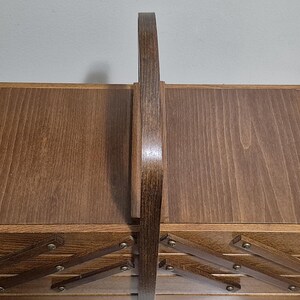 May include: A wooden sewing box with a dark brown finish. The box has a handle and a multi-tiered design with pull-out trays. The box is made of wood and has a classic, vintage aesthetic.