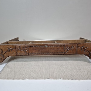 May include: A vintage wooden tray with a dark brown finish. The tray features carved floral designs on the sides and a small drawer in the center. The tray is rectangular and has several compartments.