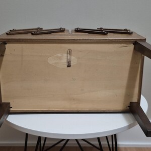 May include: A wooden, rectangular coffee table with dark brown legs and a light brown tabletop. The table is upside down, revealing the underside with a light wood finish and a small, oval-shaped sticker. The table is on a white table.