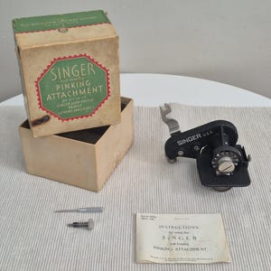 May include: A vintage Singer pinking attachment set, comprising a black metal attachment, box, and instructions. The box is tan with a green and red label. Designed for Singer lock-stitch family sewing machines.