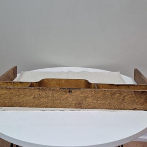 May include: A vintage wooden desk organiser with multiple compartments. The organiser is rectangular with a natural wood finish and a textured surface. It has raised sides and a central section with a curved cutout. The organiser is placed on a white surface.