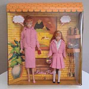May include: A vintage Barbie doll set, "Knitting Pretty," featuring two dolls in pink knit outfits. The dolls are displayed in a box with a fireplace scene backdrop. The box includes text bubbles with phrases. The set is part of the Barbie Collector series.