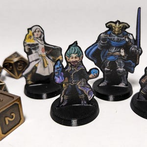 Può includere: Quattro miniature di figure fantasy su basi nere. Le figure sono una donna umana con capelli bianchi e una tunica bianca, un elfo maschio con capelli verdi e una tunica nera, un uomo umano con un elmo cornuto e un'armatura blu, e uno gnomo maschio con la barba e una tunica marrone. Le figure sono dipinte in dettaglio e sono pronte per i giochi da tavolo.
