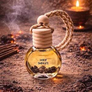 May include: A clear, round glass bottle with a wooden cap and a woven rope loop. The bottle contains a golden liquid and the text "HOLY SMOKES". The background features a candle and incense sticks, suggesting an aromatherapy product.