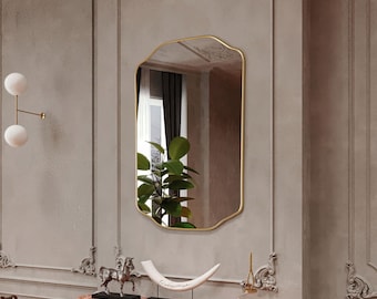 May include: A gold-framed, ornate mirror with a beveled edge hangs above a fireplace mantel. The mantel is made of red marble and features decorative carvings. A white bone sculpture sits on the mantel, and a small gold statue of a horse is on the left side of the mantel.