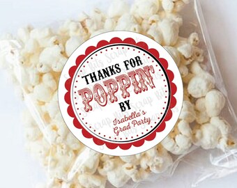 May include: Red and white circle favor tag with the text "Thanks for Poppin' by Isabella's Grad Party". The tag is attached to a clear plastic bag filled with popcorn.
