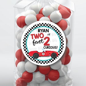 May include: A red and white favor bag with a round sticker that says "Ryan is Two fast 2 curious!" with a red race car on it. The bag is filled with red and white candy.