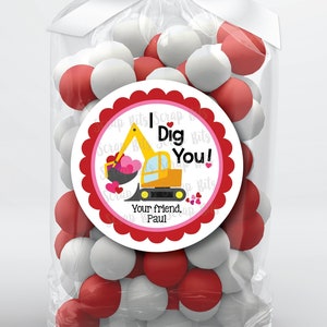 May include: A clear cellophane bag tied with a white ribbon, filled with red and white gumballs. A round sticker with a red scalloped edge features a yellow excavator and the text "I Dig You!" with the name "Paul".