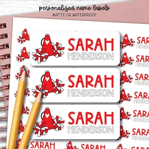 以下が含まれることがあります： 「Sarah Henderson」という名前が赤と黒の文字で印刷された、長方形のパーソナライズされた名前ラベルのシート。各ラベルには、白いハートが付いた赤いメガホンと、赤と白のポンポンが描かれています。ラベルはマットまたは防水仕様です。