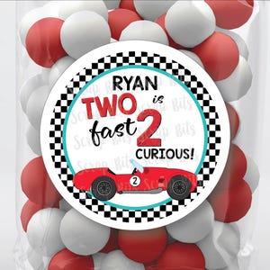 May include: A round sticker with a checkered black and white background. The sticker has a red race car with the number 2 on it. The text on the sticker reads "Ryan is Two fast 2 curious!"