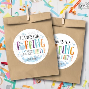 May include: Two brown paper bags with round white stickers that say "Thanks for Popping by my Birthday Party!" with colorful bubble illustrations and the name Avery.
