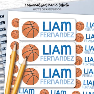 May include: A sheet of rectangular personalised name labels featuring a basketball graphic and the text LIAM FERNANDEZ in blue. The labels are matte or waterproof. The sheet includes multiple labels of varying sizes, some with basketballs and some with text.