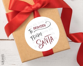 May include: A round white gift tag with black and red text that reads To: Brayden From: Santa, centered on a brown cardboard gift box wrapped with a bright red satin ribbon. The tag features a decorative script font for the names and labels.