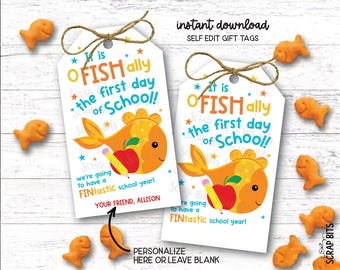 Op de afbeelding: Twee witte rechthoekige cadeaulabels met afgeronde bovenkanten en bruine touwstrikjes. Elk label toont een cartoon goudvis die een rode appel en een geel potlood vasthoudt, met de tekst: It is FISH ally the first day of School! we're going to have a FINtastic school year!