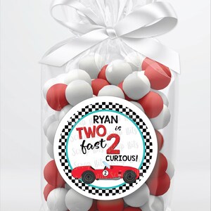 May include: A red and white checkered circle favor tag with a red race car and the text "Ryan is Two fast 2 curious!"  The tag is attached to a clear cellophane bag filled with red and white candy.