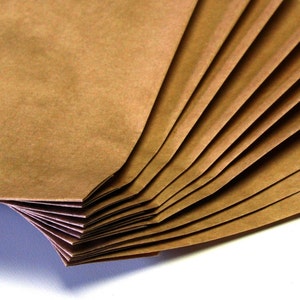 Op de afbeelding: Een stapel bruine papieren zakken gevouwen in een waaier. De zakken zijn gemaakt van getextureerd papier en hebben een natuurlijke, rustieke uitstraling.