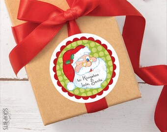 Könnte beinhalten: Ein runder Aufkleber mit einem Cartoon-Weihnachtsmann, der eine rote Mütze mit Stechpalme trägt, vor einem grünen Hintergrund mit Punkten und einem roten Wellenrand. Der Text lautet: to: Kingston love, Santa. Der Aufkleber klebt auf einer braunen Geschenkbox.