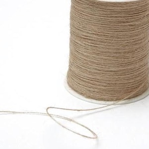 May include: A spool of natural-colored twine sits on a white surface. The twine is tightly wound around a white cardboard core. A length of twine extends from the spool, forming a loop. The twine has a rough, textured appearance.