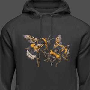 May include: A black hooded sweatshirt featuring a detailed illustration of two bumblebees. The bees are depicted with yellow, black, and white markings, with intricate wing details. The hoodie has a drawstring and a kangaroo pocket.
