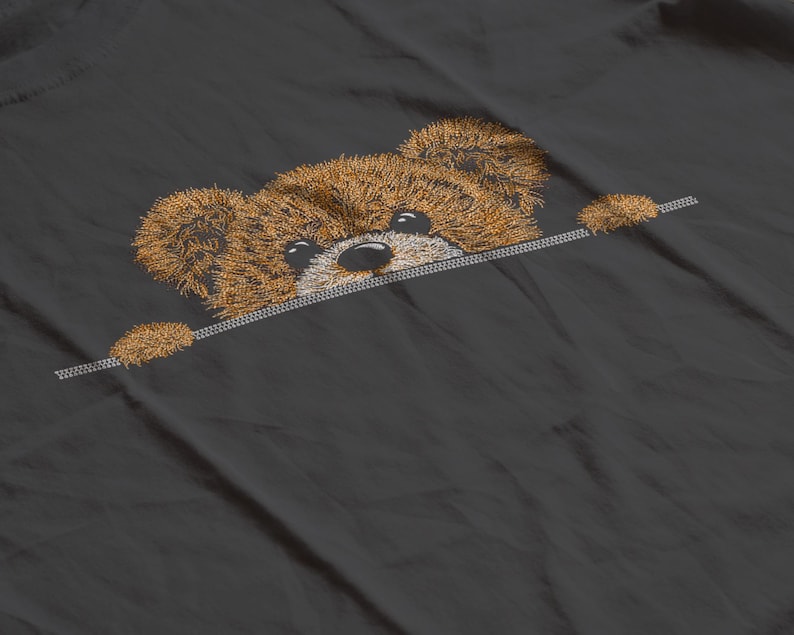 May include: Embroidered brown teddy bear peeking over a silver line on a dark gray fabric. The bear has a fluffy texture with black eyes and a black nose. The design is detailed and appears to be stitched.